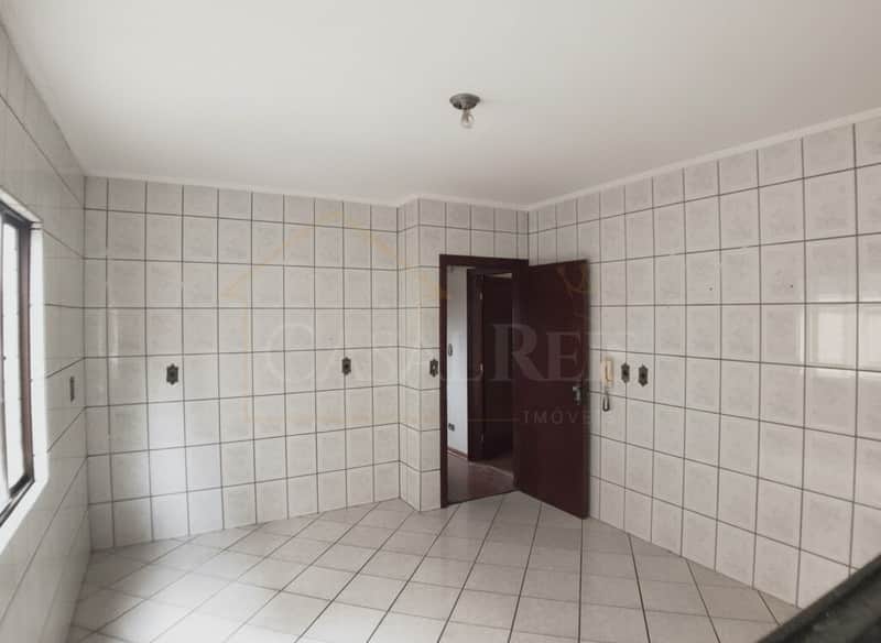 Cozinha ampla com azulejos claros, porta de madeira escura e piso cerâmico. Ambiente iluminado e arejado.