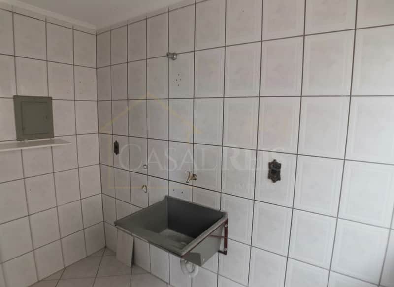 Área de serviço com tanque cinza, azulejos brancos e instalações aparentes. Ambiente funcional.