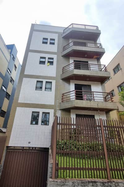 Fachada de prédio com sacadas e revestimento em azulejo. Portão marrom e cerca de metal na frente.