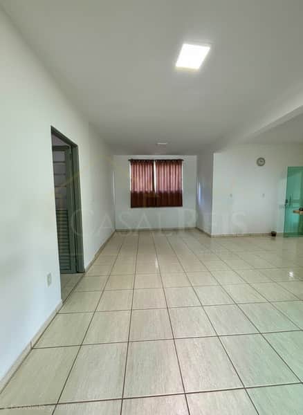 Sala ampla e iluminada com piso cerâmico claro e cortinas marrons na janela.