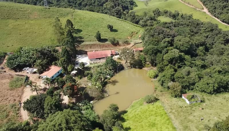 Vista aérea de fazenda com lago, casa com telhado vermelho e muita área verde.