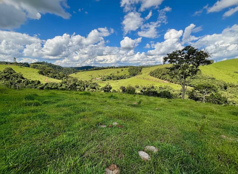 Área externa com gramado verde, morros e céu azul com nuvens. Paisagem rural ensolarada.