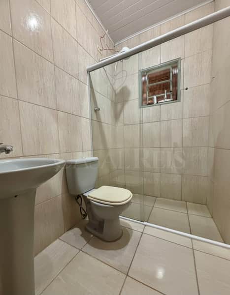 Banheiro com pia, vaso sanitário e box de vidro com janela. Revestimento em cerâmica bege.