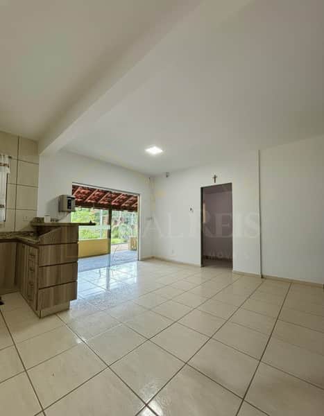 Sala ampla com piso claro, armários de cozinha e acesso à área externa com telhado. Porta para outro ambiente.