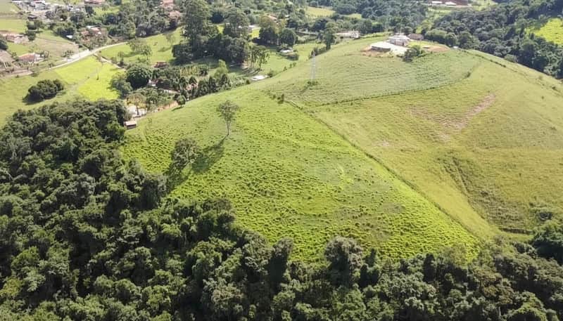 Área externa com morro gramado, árvores e construções ao fundo. Paisagem ensolarada e natural.