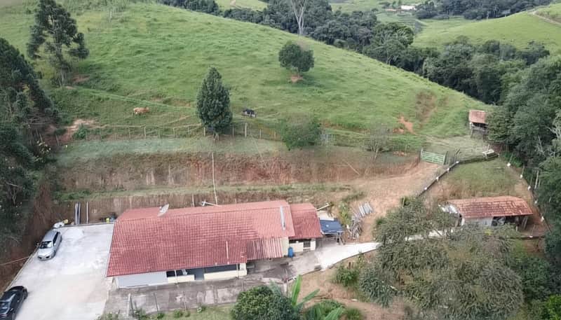 Vista aérea de propriedade rural. Casa térrea com telhado vermelho, pasto verde e árvores ao redor.