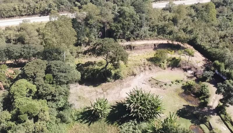 Área externa com vegetação densa, lago seco e estrada ao fundo. Vista aérea ensolarada.