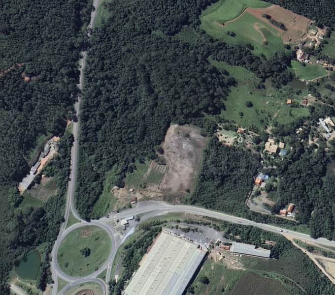Vista aérea de área rural com floresta densa, pastagens, casas e rodovia com trevo.