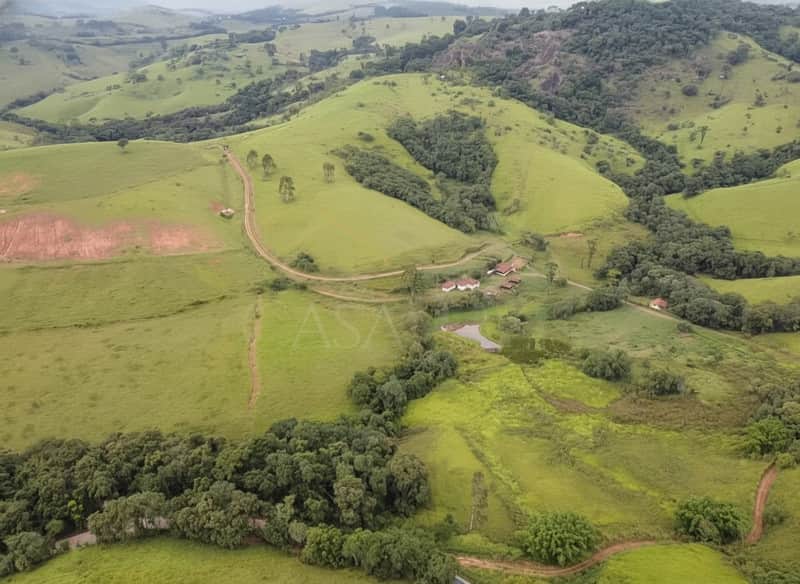 Fazenda verdejante com casas, lago e montanhas. Vista aérea da área externa rural.