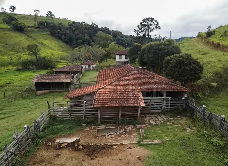 Casa antiga em fazenda. Telhado rústico, cerca de madeira e paisagem verde. Área externa campestre.