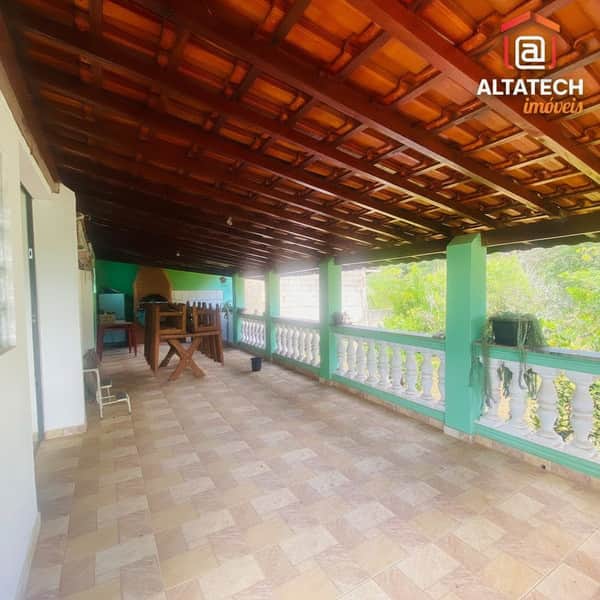 Varanda ampla com piso cerâmico, churrasqueira, guarda-corpo branco e vista para a natureza.