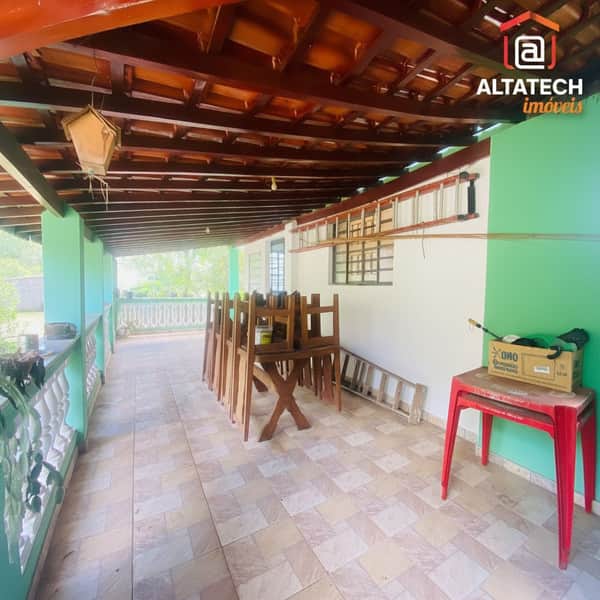 Varanda ampla com piso cerâmico, teto de madeira, cadeiras empilhadas e mesa rústica.