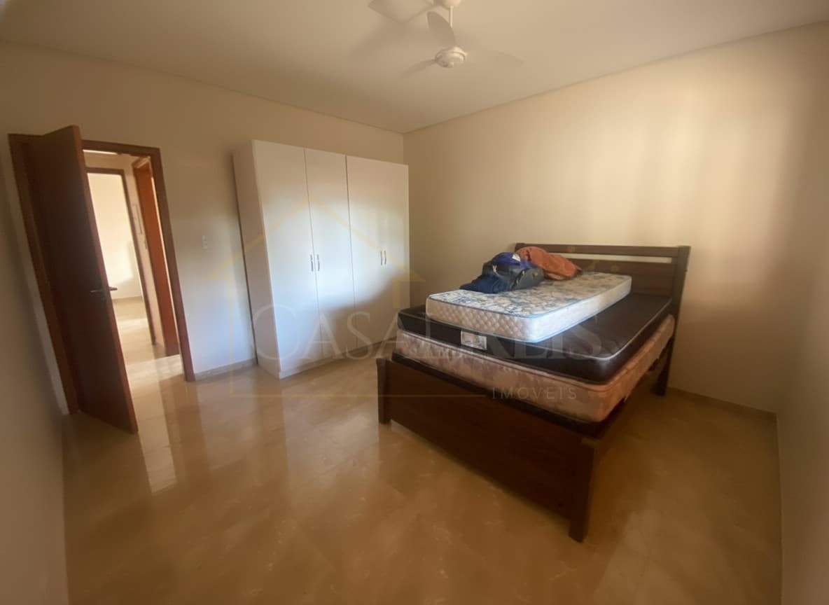 Quarto amplo com cama de madeira, armário branco e piso claro. Ambiente iluminado e arejado.