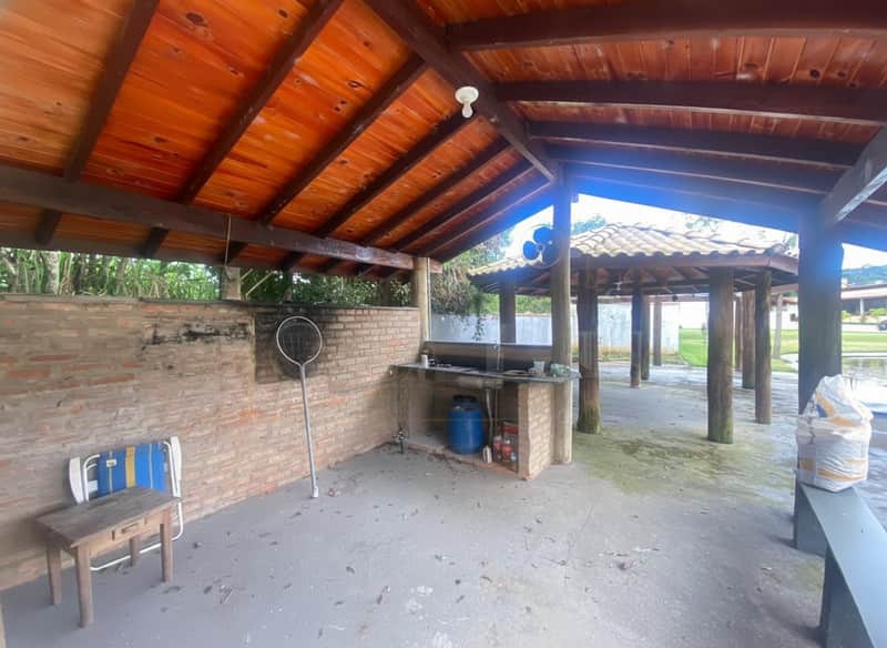 Área externa com churrasqueira de tijolos, bancada e estrutura de madeira rústica. Ambiente amplo e arejado.