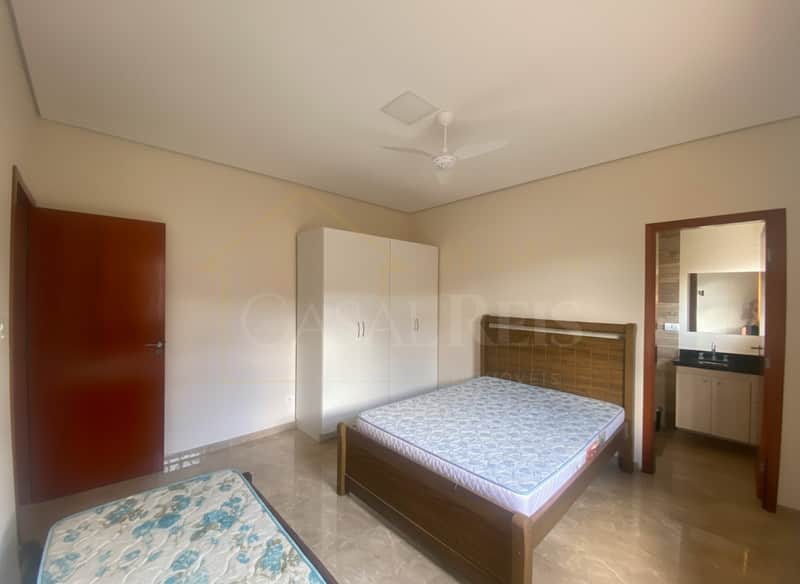 Quarto com duas camas, armário branco e porta para banheiro. Piso claro e iluminação central.