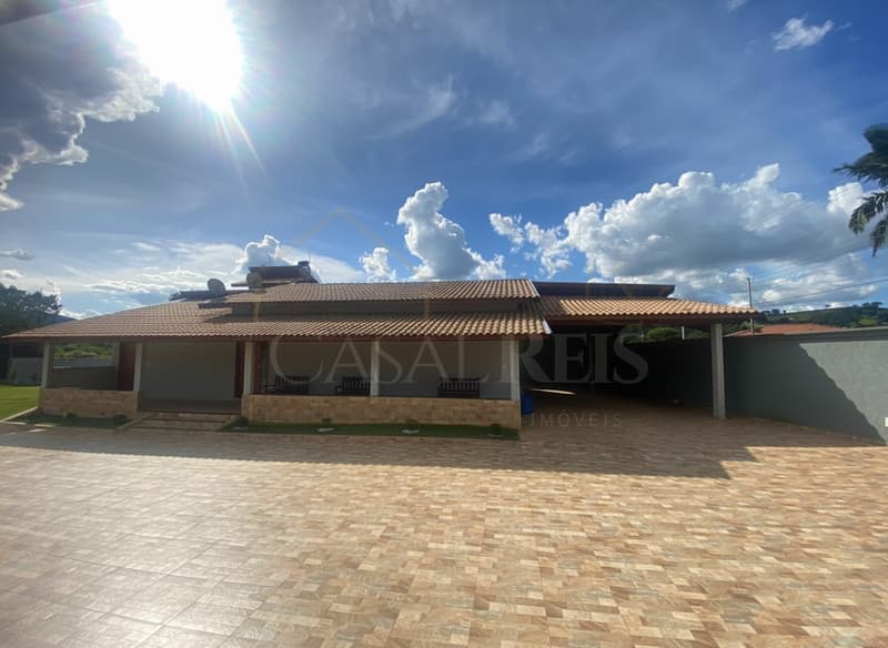 Fachada de casa térrea com varanda e garagem. Piso em cerâmica e céu azul com nuvens.