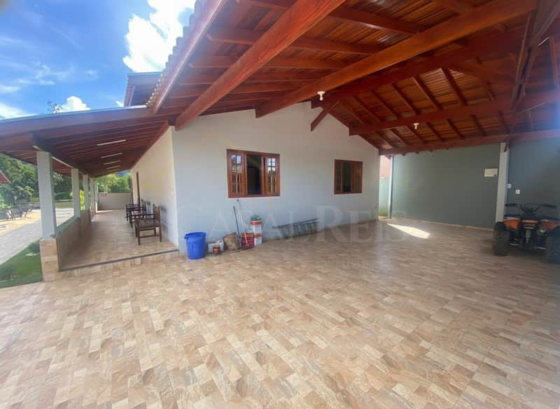 Área externa ampla com piso cerâmico, casa com janelas de madeira e teto amadeirado.