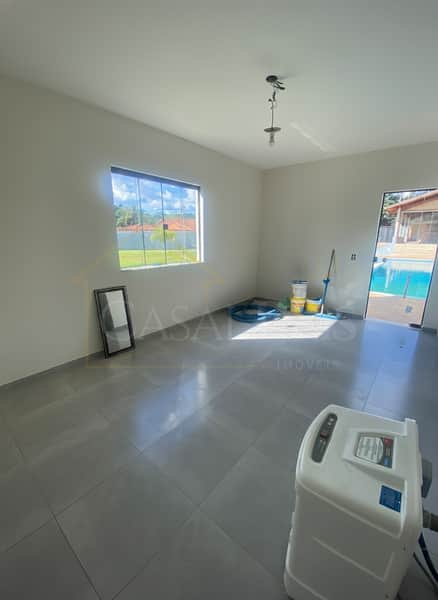 Sala ampla com piso cinza, janela com vista para o jardim e piscina ao fundo.
