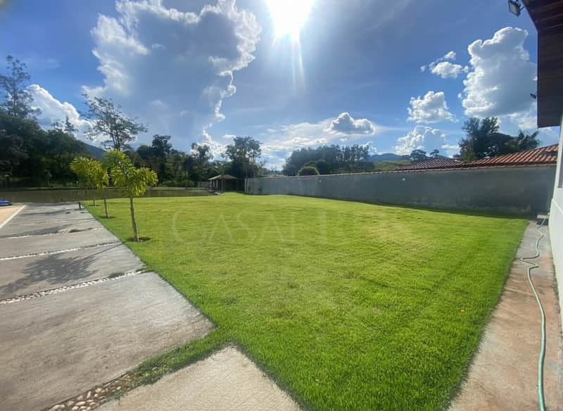 Ampla área externa com gramado verde e bem cuidado em dia ensolarado. Paisagem natural ao fundo.