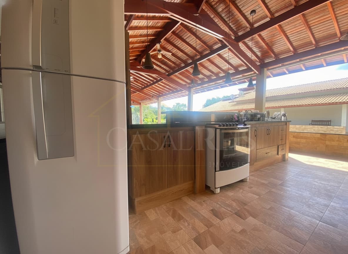 Cozinha ampla com armários de madeira, geladeira branca e forno. Área externa com teto de madeira.