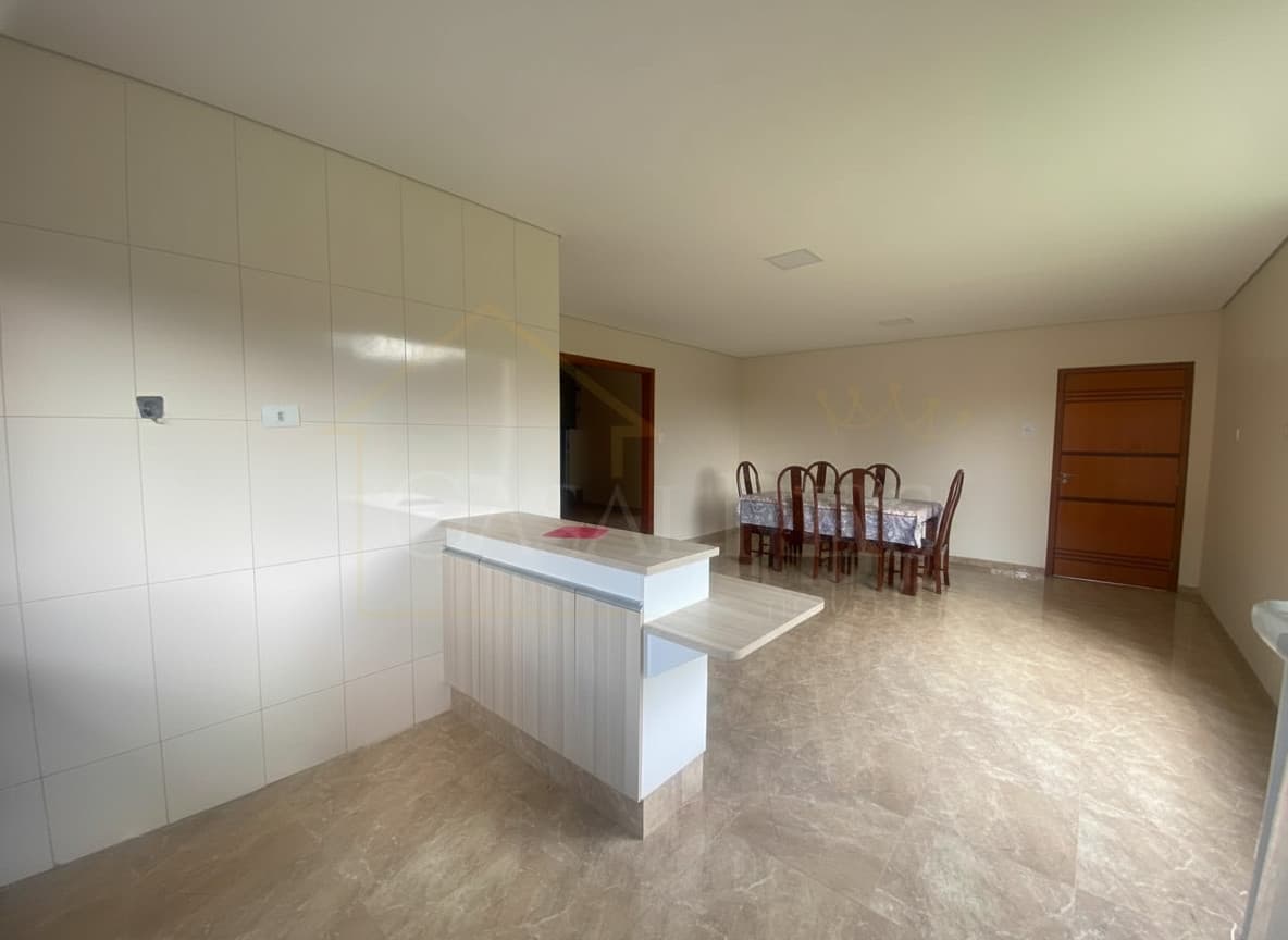 Sala de jantar ampla com mesa, cadeiras e balcão com revestimento claro. Piso em porcelanato brilhante.