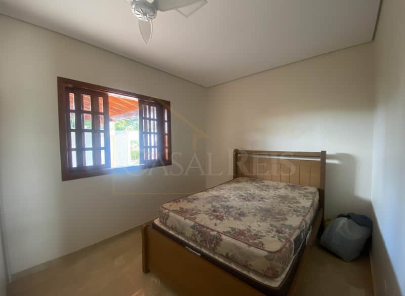 Quarto com cama de madeira, janela aberta e piso claro. Ambiente iluminado e arejado.