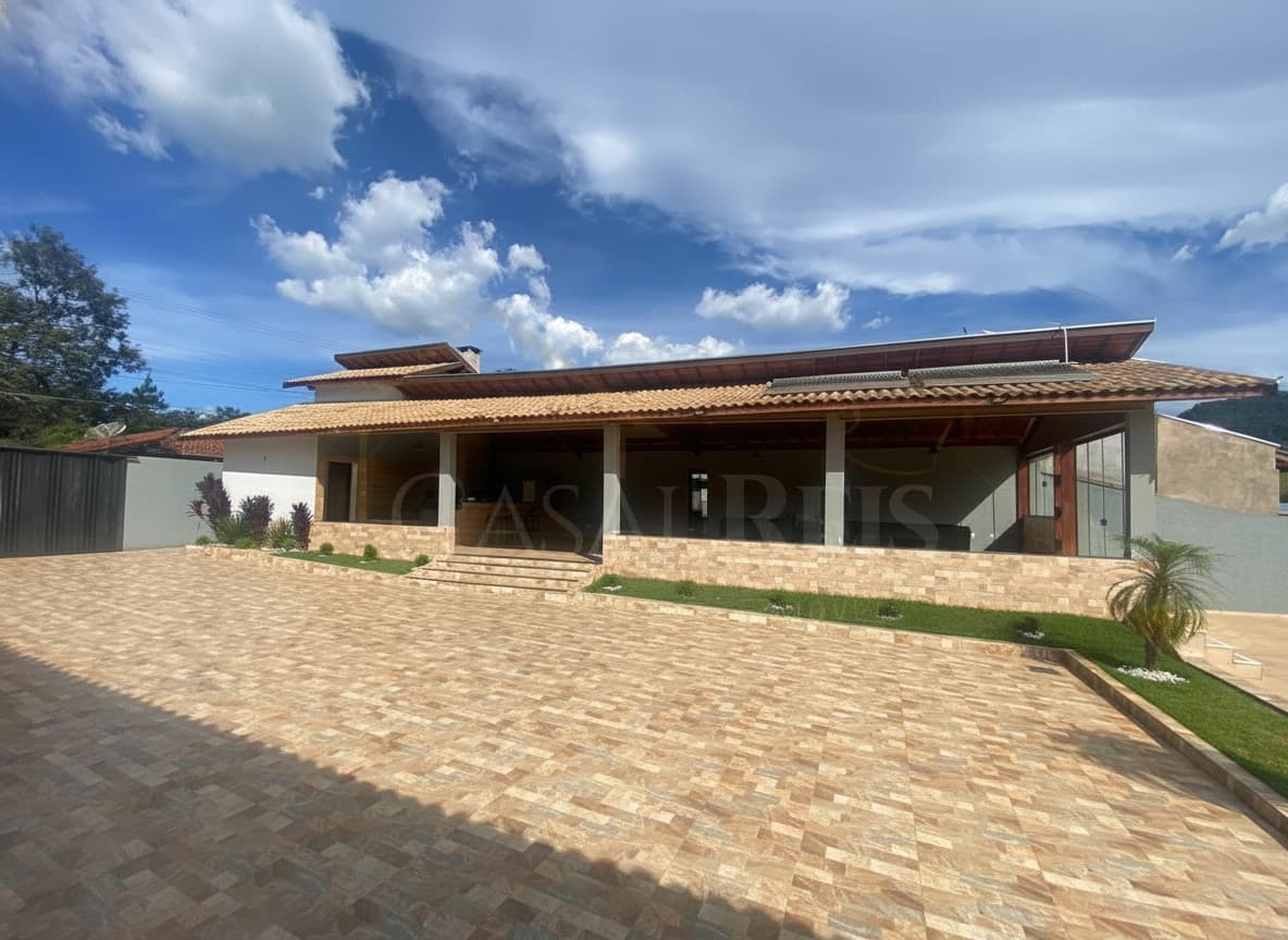 Fachada de casa térrea com área externa ampla e piso cerâmico. Destaque para o céu azul com nuvens.