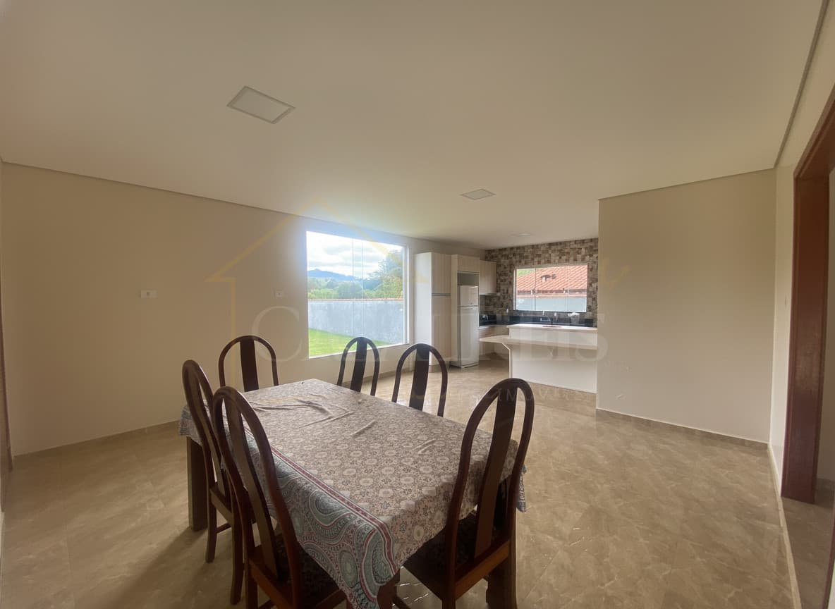 Sala de jantar ampla e iluminada, com mesa e cadeiras de madeira. Cozinha americana ao fundo.