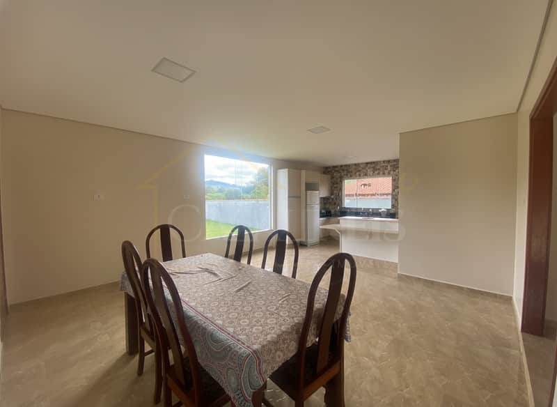 Sala de jantar ampla e iluminada, com mesa e cadeiras de madeira. Cozinha americana ao fundo.