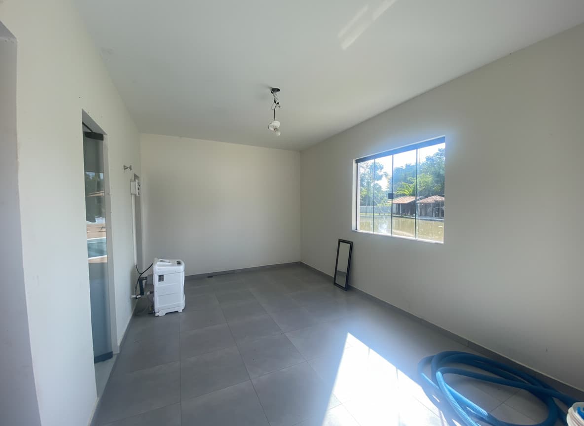 Sala ampla e clara com piso cinza, janela com vista para lago e paredes brancas.