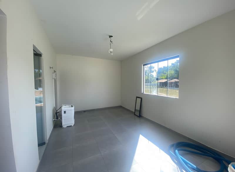 Sala ampla e clara com piso cinza, janela com vista para lago e paredes brancas.