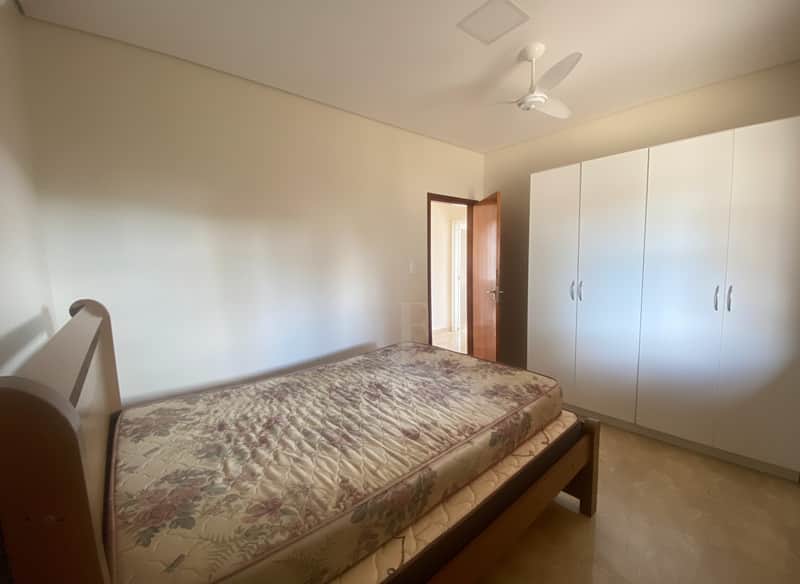 Quarto com cama de madeira, armário branco e piso bege. Ambiente iluminado e arejado.