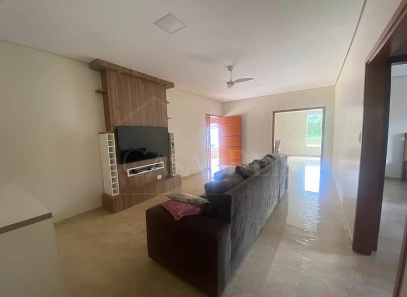 Sala ampla e iluminada com TV, sofá moderno e piso brilhante. Decoração clean e porta colorida ao fundo.