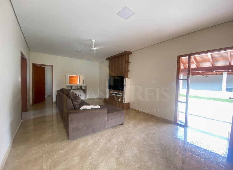 Sala ampla com sofá marrom, piso claro e porta para área externa com gramado. Decoração minimalista.